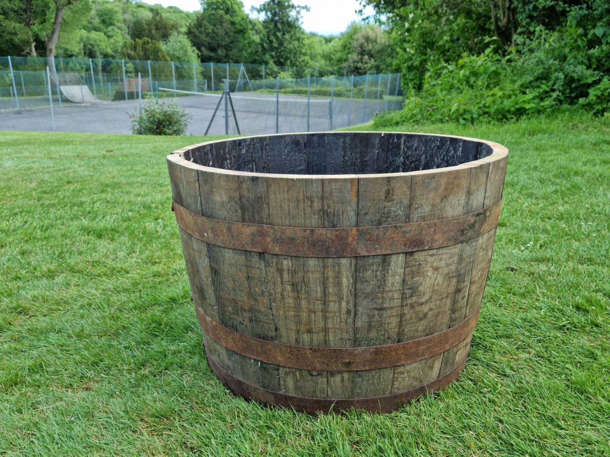 Wooden barrel planter on grass with tennis court in the background
