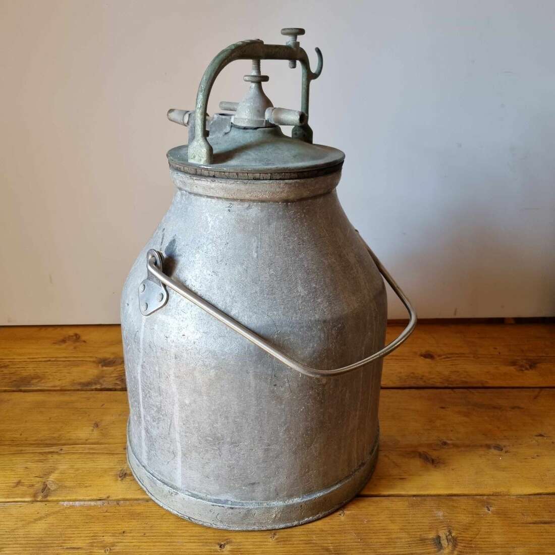 Vintage metal milk churn on a wooden floor with a plain wall background