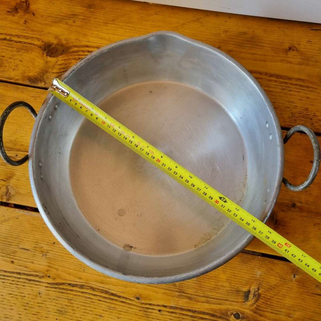 Metal pan on a wooden surface with a measuring tape indicating its diameter.