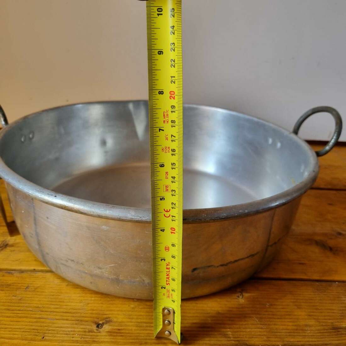 Metal pot on a wooden surface with a measuring tape indicating its height.