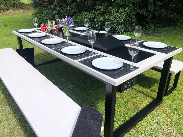 Outdoor dining table set with plates, glasses, and cutlery on a grassy area.