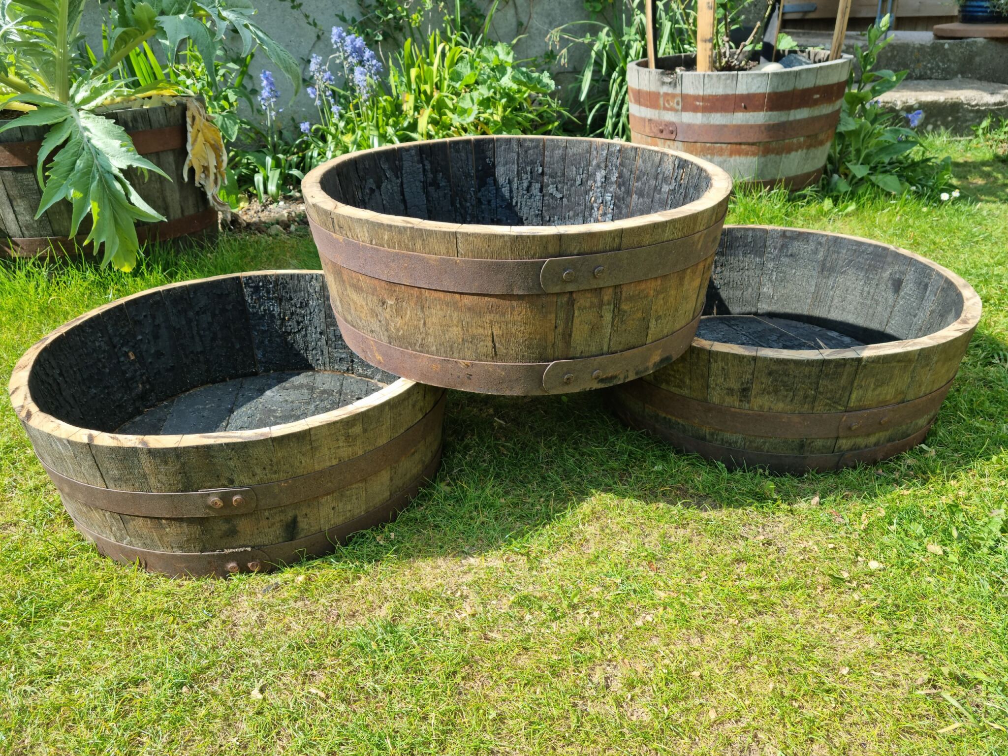 Three wooden planters on grass with a garden background