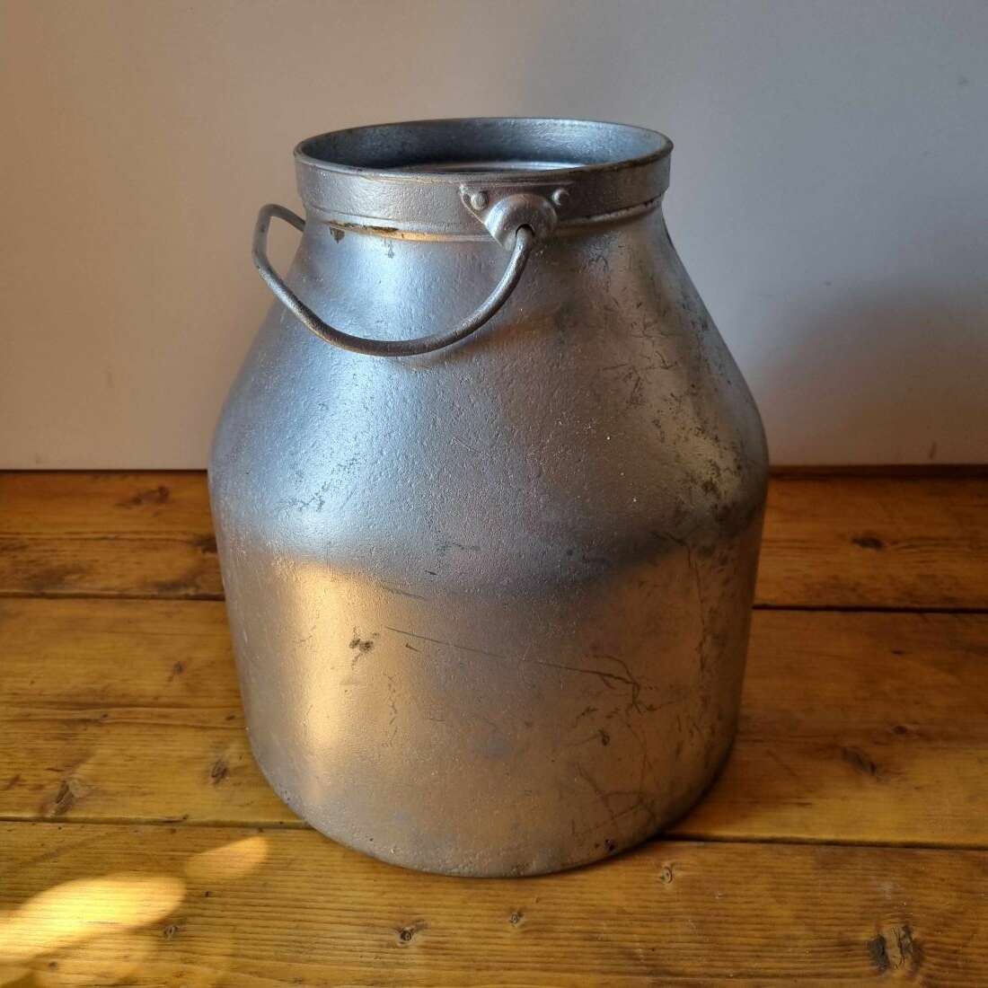 Vintage metal milk churn on a wooden surface with a plain background