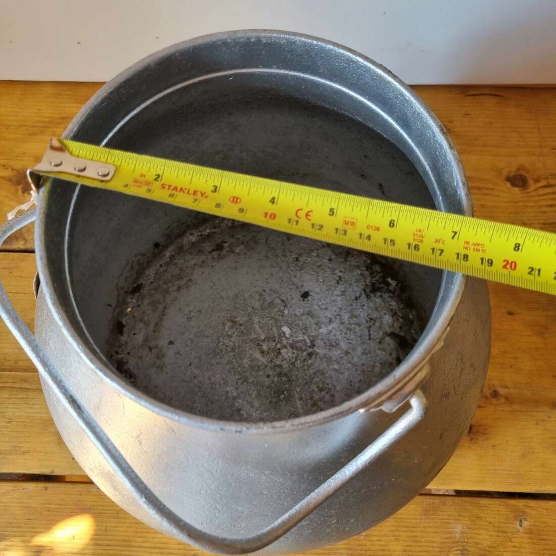 Metal bucket with a measuring tape showing its dimensions on a wooden surface.