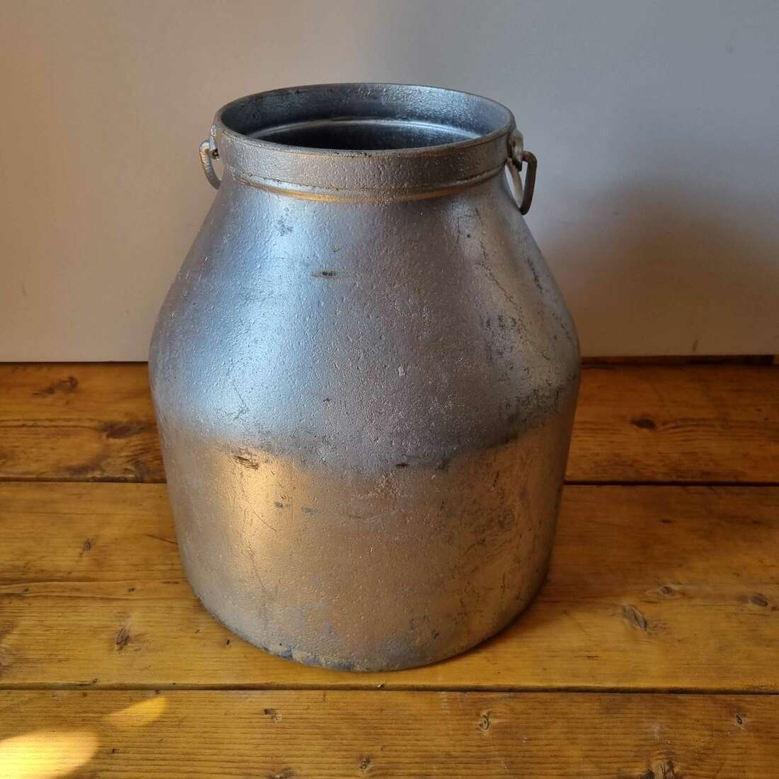 Vintage metal milk churn on a wooden surface with a plain background