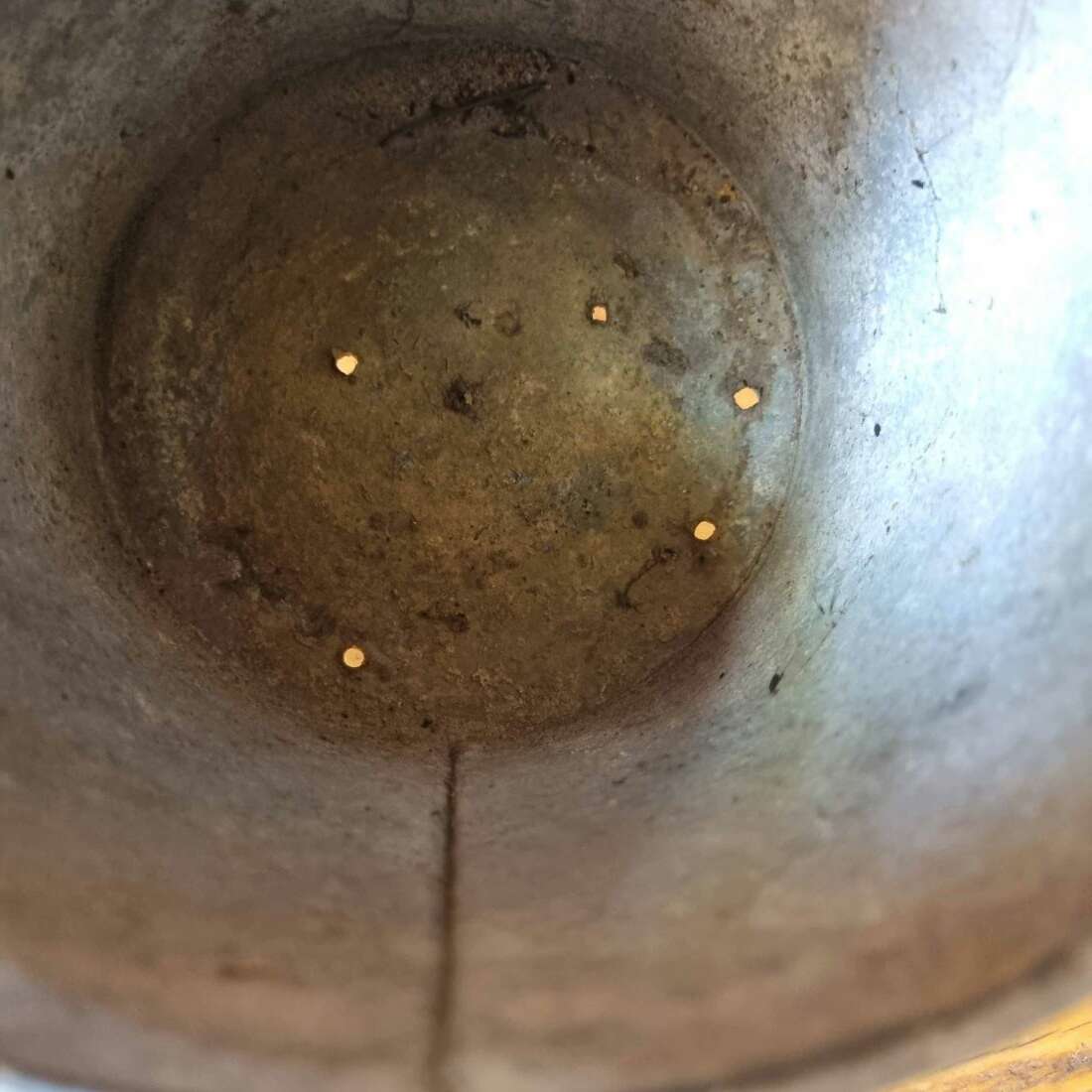 Close-up of a metal bowl with a circular depression and small holes inside.