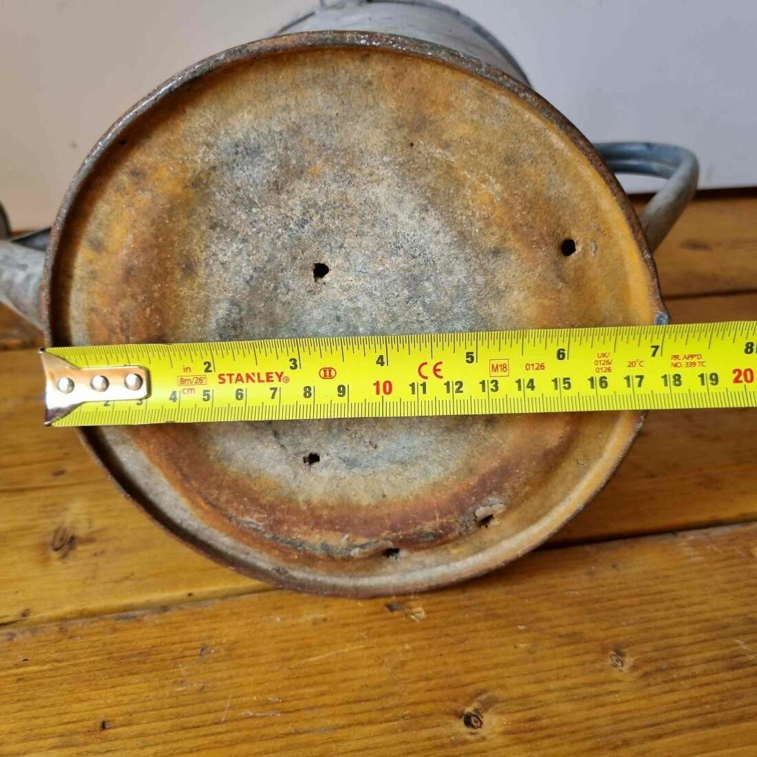 Vintage metal object with a measuring tape indicating its diameter on a wooden surface.
