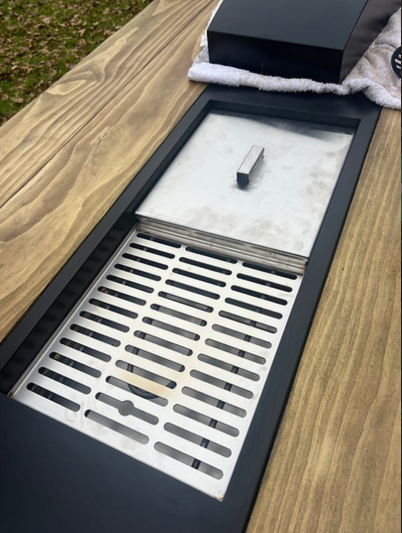 Metallic grill on a wooden surface with a black box and white towel in the background.