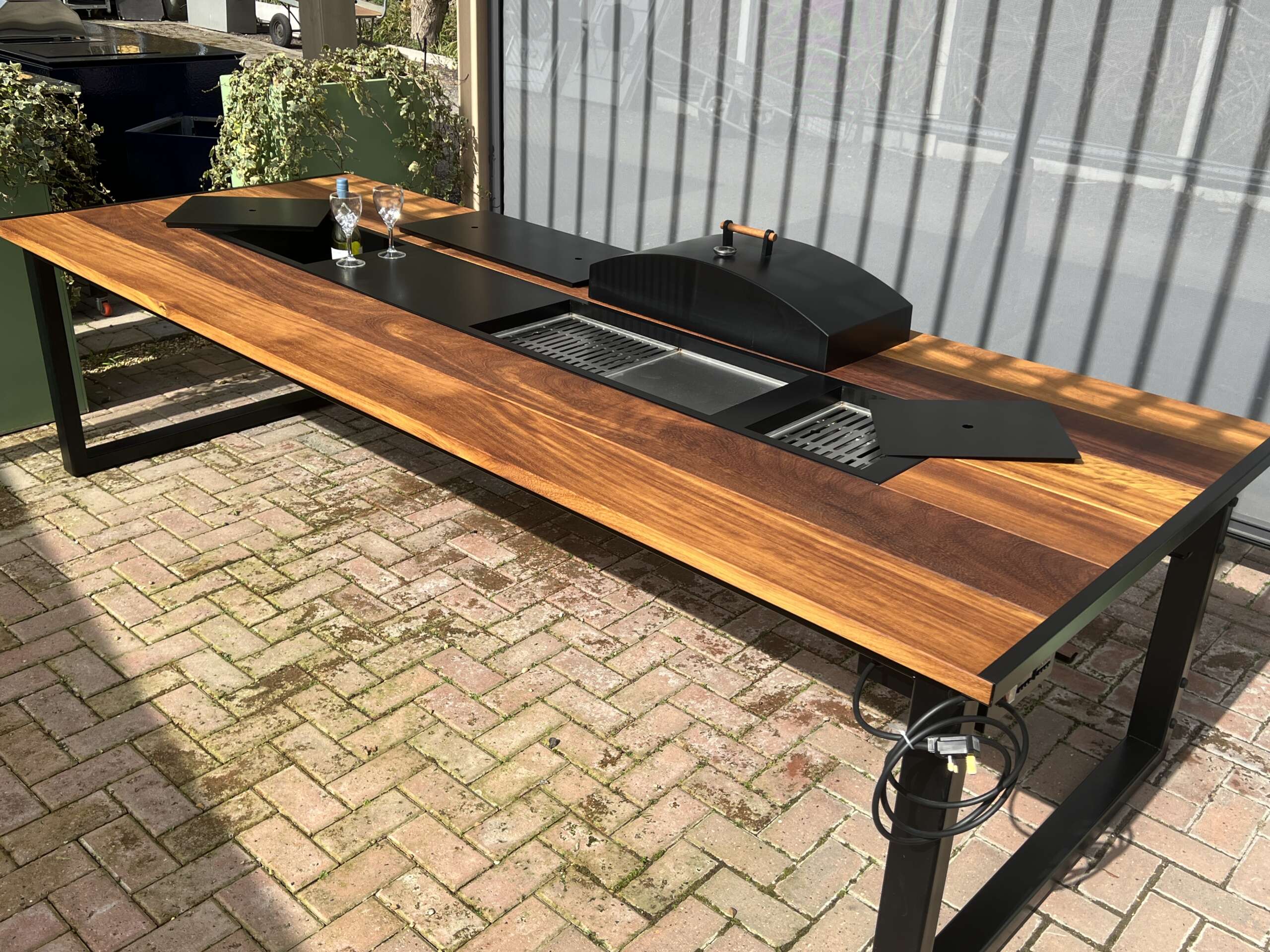 Outdoor kitchen counter with wooden top and black appliances on a brick patio.