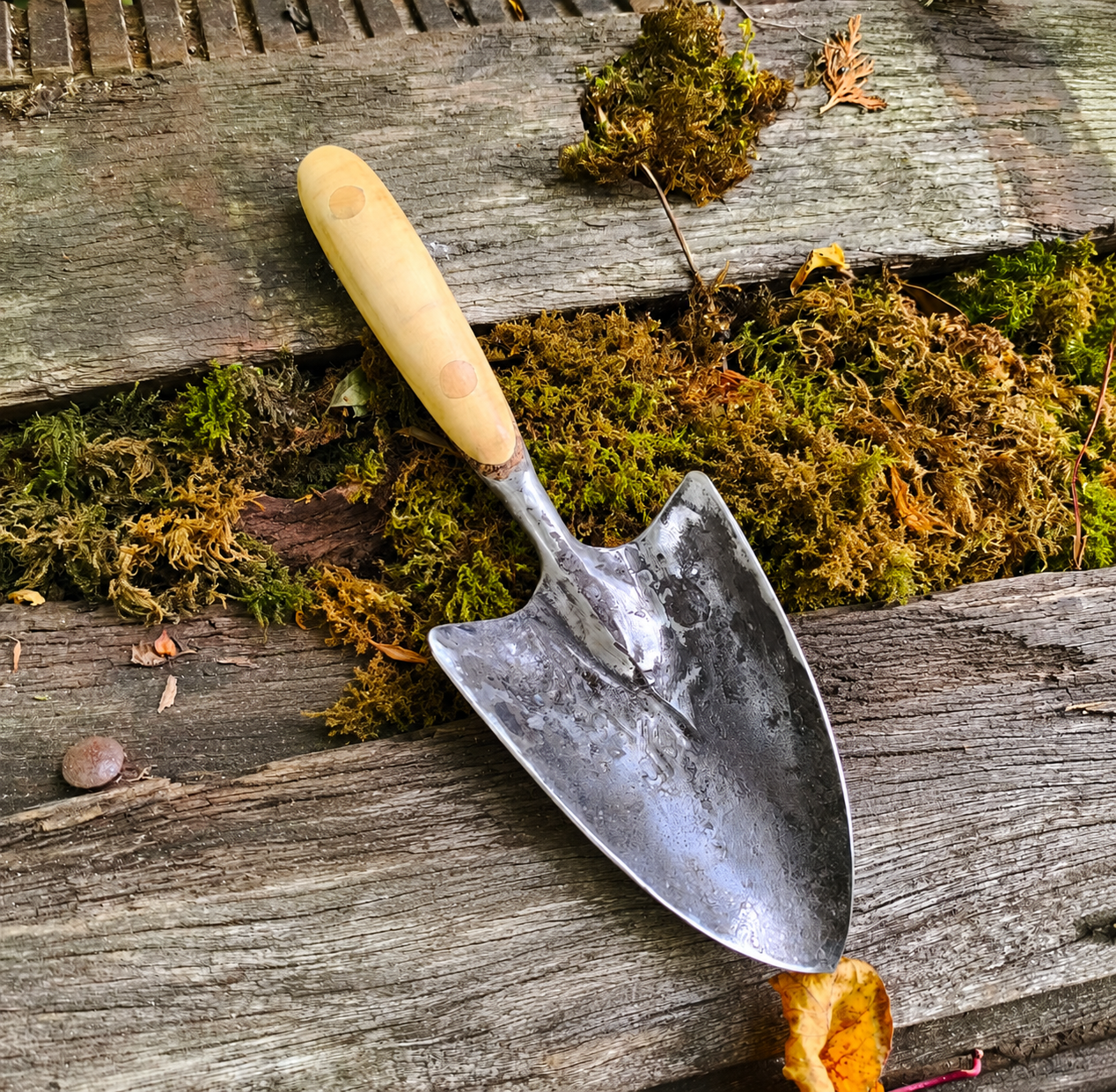 British hand forged garden trowel by The Anvil & Yew resting on weathered timber and moss