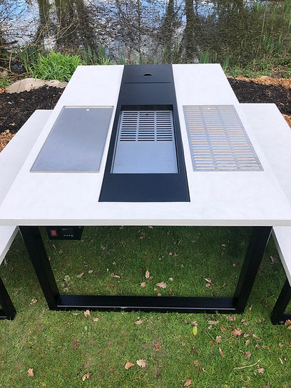 Outdoor table with built-in electronic components on a grassy area near water.