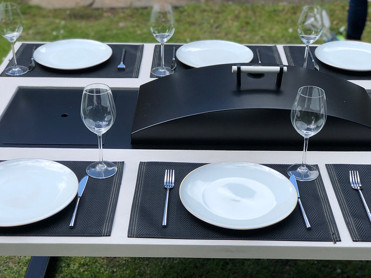 Dining table set with plates, glasses, and cutlery on a grassy outdoor setting.