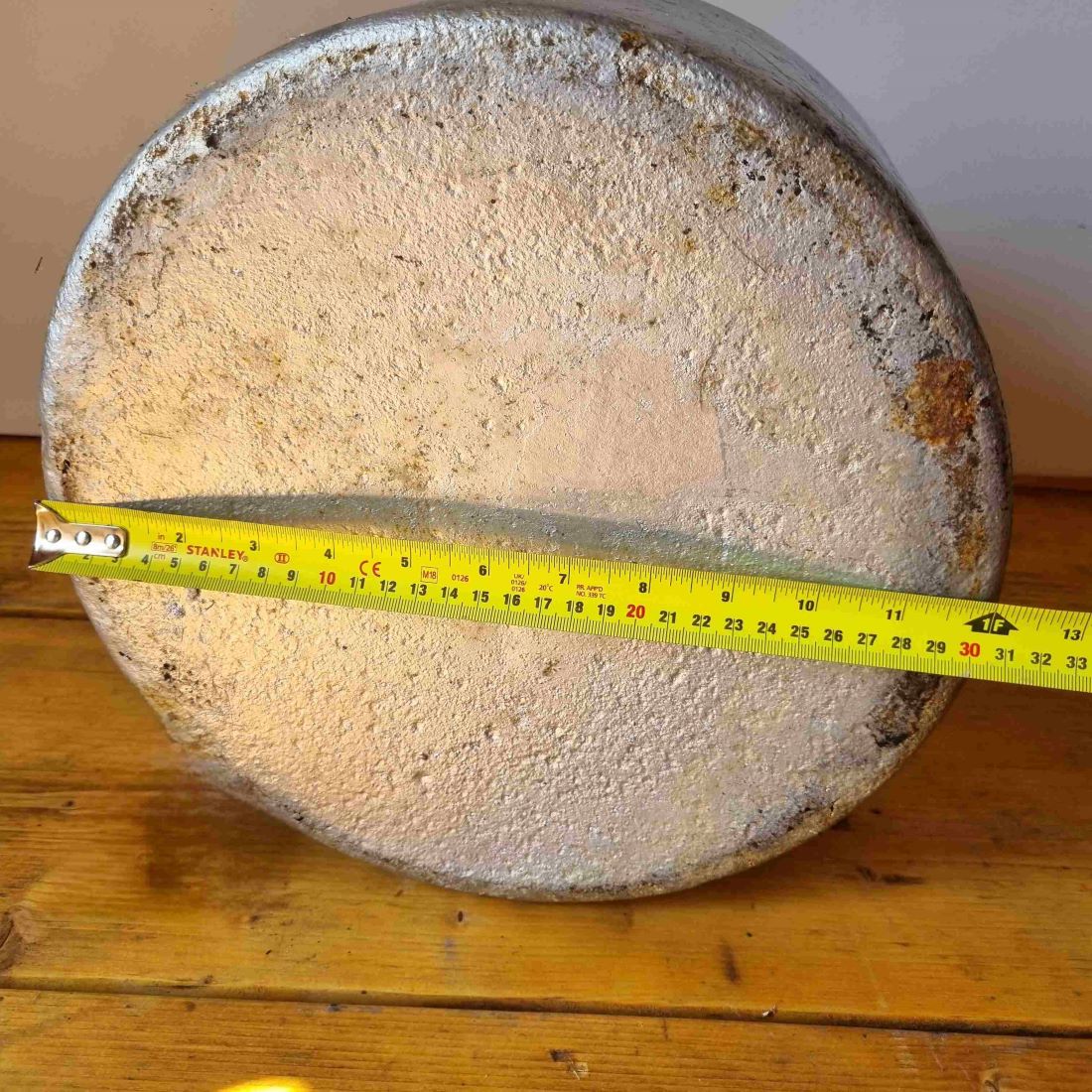 Round concrete block with a measuring tape indicating its size on a wooden surface.