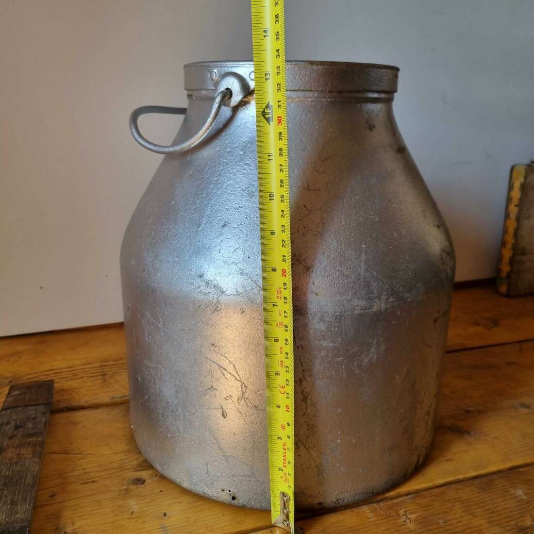 Two metal jugs on a wooden surface with a measuring tape for scale.